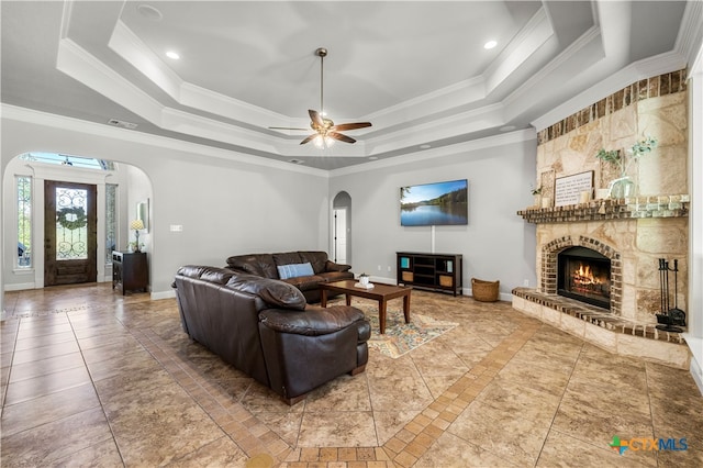 living room featuring ceiling fan, a tray ceiling, ornamental molding, and a fireplace