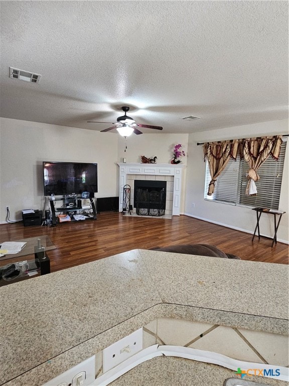 living room with a textured ceiling, hardwood / wood-style flooring, ceiling fan, and a tiled fireplace