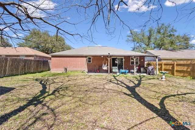 rear view of property featuring a yard, brick siding, a patio, and a fenced backyard