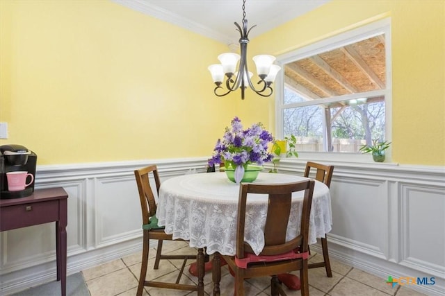 dining space with ornamental molding, a wainscoted wall, a notable chandelier, and light tile patterned flooring