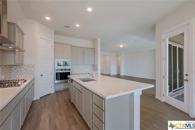 kitchen featuring stainless steel appliances, a center island with sink, sink, backsplash, and light wood-type flooring