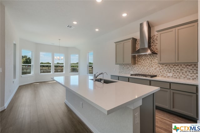 kitchen featuring an island with sink, wall chimney exhaust hood, and stainless steel gas stovetop