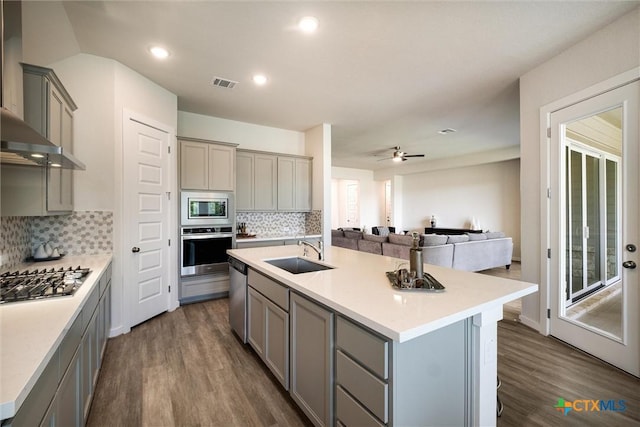 11305 Hollering Pass, Schertz, TX 78154 - kitchen with gray cabinets, stainless steel appliances, wall chimney exhaust hood, backsplash, and dark wood-style floors