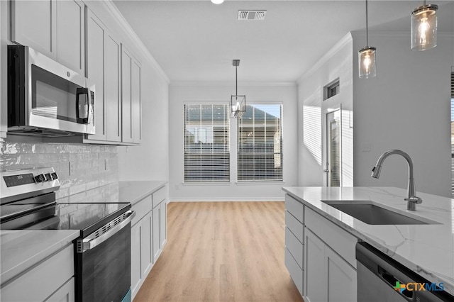 kitchen with light wood finished floors, tasteful backsplash, stainless steel appliances, crown molding, and a sink