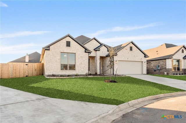 french country inspired facade with a garage, concrete driveway, fence, and a front lawn