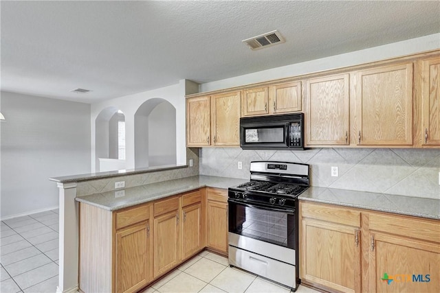 kitchen with light tile patterned flooring, light brown cabinets, stainless steel range with gas stovetop, kitchen peninsula, and backsplash