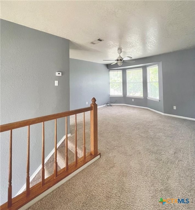 empty room with carpet flooring, ceiling fan, and a textured ceiling