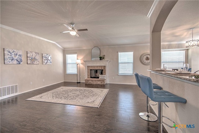 living room featuring a wealth of natural light, a brick fireplace, dark wood-style floors, and ceiling fan with notable chandelier