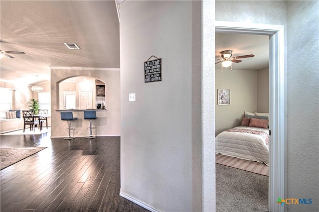 hall with visible vents, arched walkways, dark wood-style flooring, and a textured wall