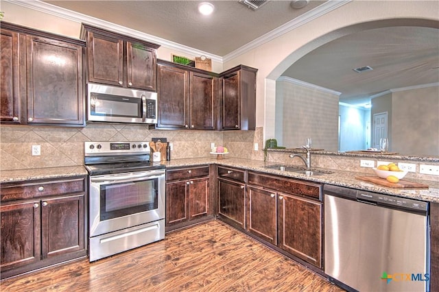 kitchen with arched walkways, a sink, dark brown cabinets, appliances with stainless steel finishes, and light stone countertops