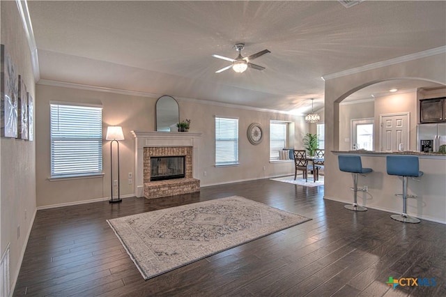 living room with dark wood-style floors, a brick fireplace, a ceiling fan, and crown molding