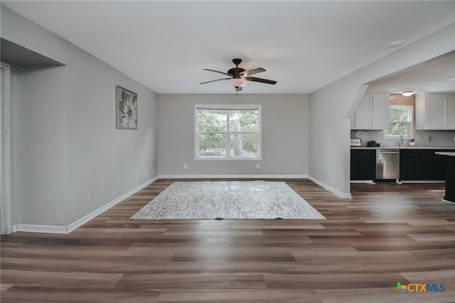 unfurnished living room with a ceiling fan, baseboards, a sink, and dark wood-style floors