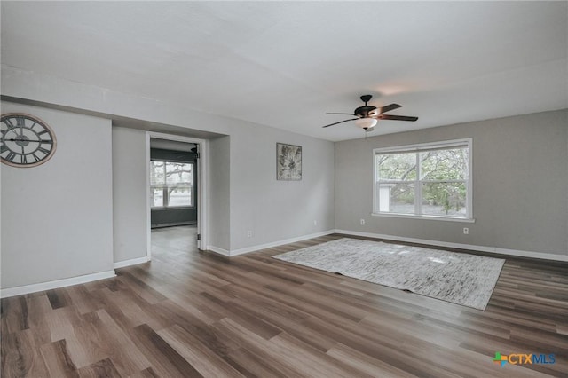 unfurnished room with ceiling fan, a wealth of natural light, wood finished floors, and baseboards
