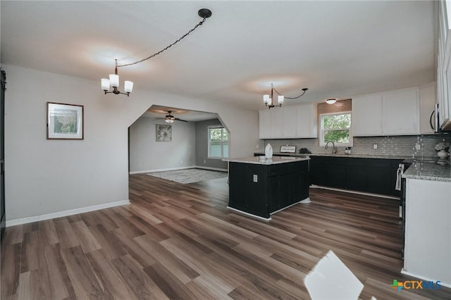 kitchen featuring white cabinets, tasteful backsplash, ceiling fan with notable chandelier, dark cabinetry, and a kitchen island