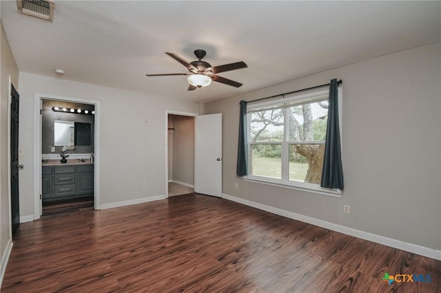unfurnished bedroom with connected bathroom, baseboards, and dark wood-style flooring