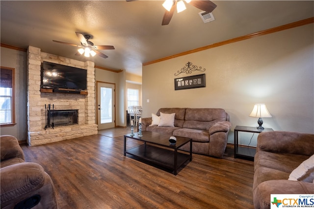 living room with ceiling fan, dark hardwood / wood-style floors, a stone fireplace, and ornamental molding