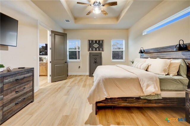 bedroom featuring a tray ceiling, light hardwood / wood-style flooring, ceiling fan, and ensuite bathroom