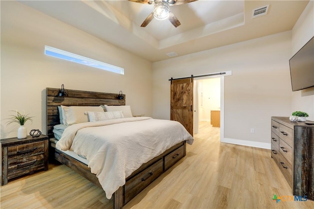 bedroom featuring ceiling fan, a barn door, light hardwood / wood-style floors, and a tray ceiling