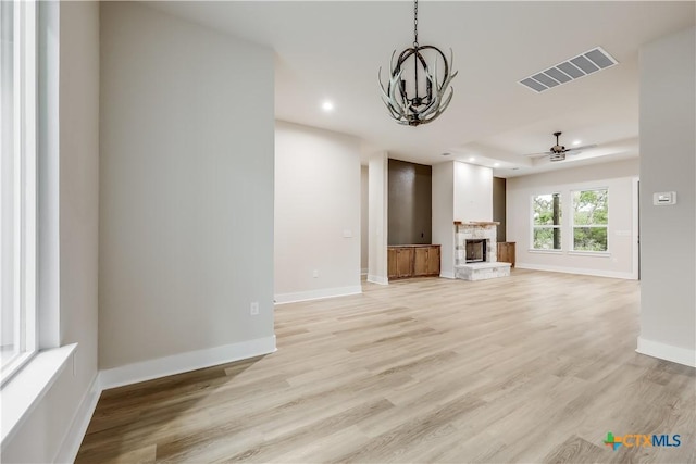 unfurnished living room featuring a fireplace, ceiling fan with notable chandelier, and light hardwood / wood-style floors