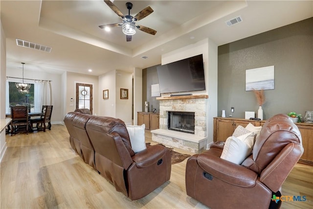 living room with a raised ceiling, light hardwood / wood-style floors, and ceiling fan with notable chandelier