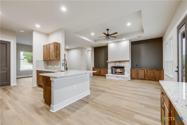 kitchen with ceiling fan, sink, a raised ceiling, light hardwood / wood-style flooring, and a fireplace