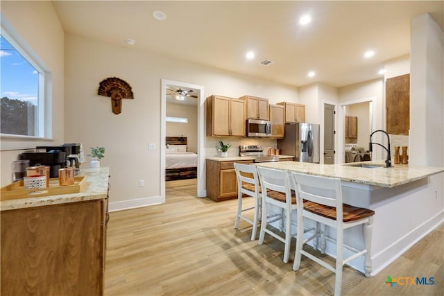 kitchen with kitchen peninsula, a kitchen breakfast bar, stainless steel appliances, sink, and light hardwood / wood-style floors