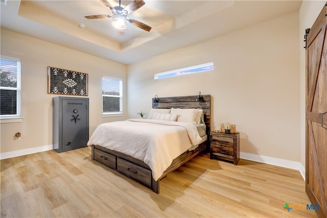 bedroom with a raised ceiling, a barn door, ceiling fan, and light hardwood / wood-style floors