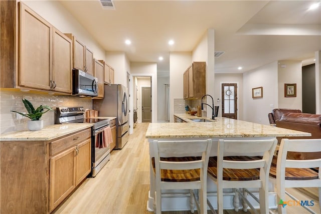 kitchen featuring sink, kitchen peninsula, a breakfast bar, appliances with stainless steel finishes, and light wood-type flooring