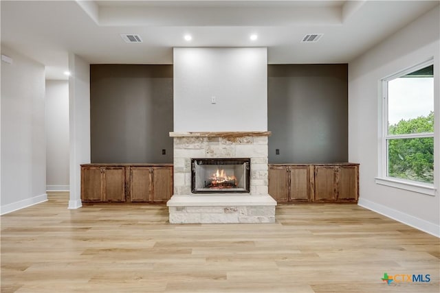 unfurnished living room featuring light wood-type flooring, a tray ceiling, and a stone fireplace