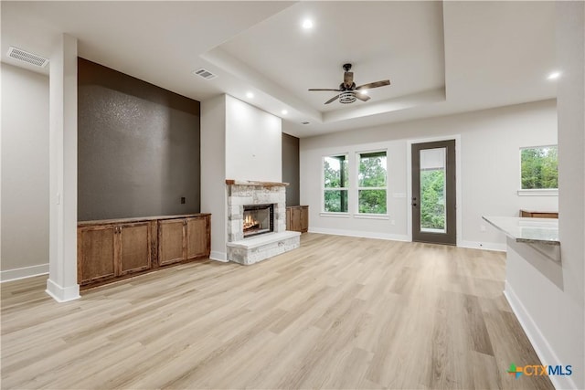 unfurnished living room featuring a tray ceiling, ceiling fan, and light wood-type flooring