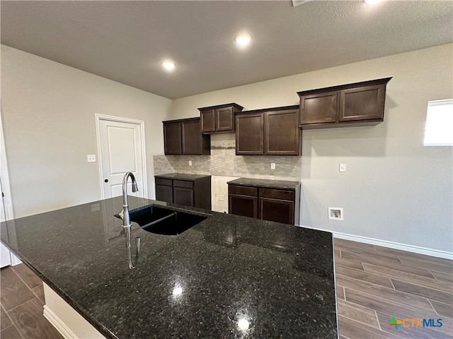 kitchen with a sink, dark brown cabinetry, a large island with sink, wood tiled floors, and recessed lighting