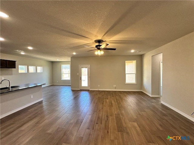 unfurnished living room featuring a ceiling fan, dark wood finished floors, a textured ceiling, baseboards, and a sink