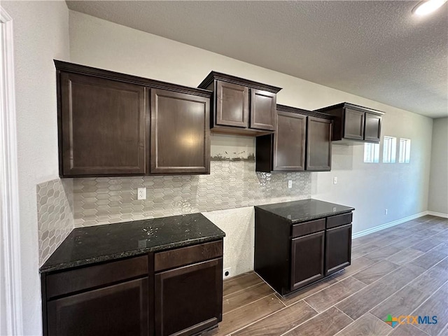 kitchen featuring dark brown cabinetry, dark stone counters, decorative backsplash, a textured ceiling, and dark wood-style floors