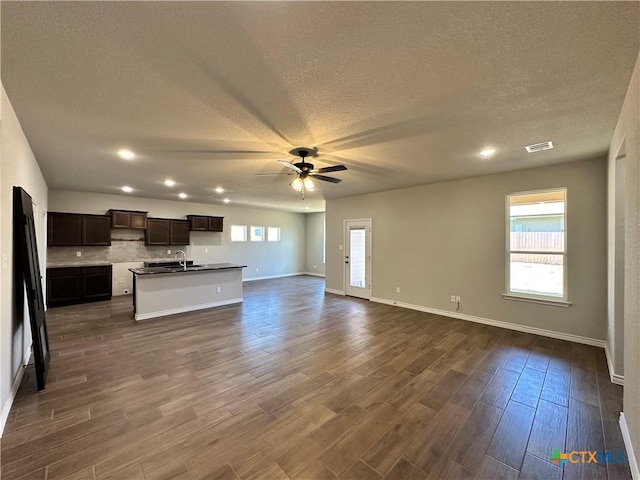kitchen with open floor plan, ceiling fan, a sink, a textured ceiling, and an island with sink