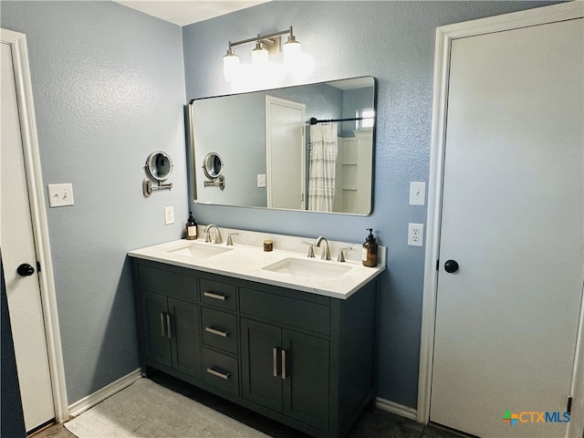 bathroom featuring a textured wall, double vanity, baseboards, and a sink