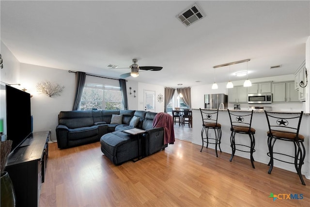 living area featuring light wood-style floors, ceiling fan, visible vents, and a wealth of natural light
