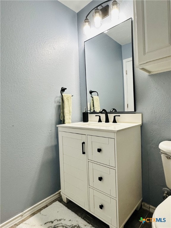 half bathroom featuring toilet, vanity, and baseboards