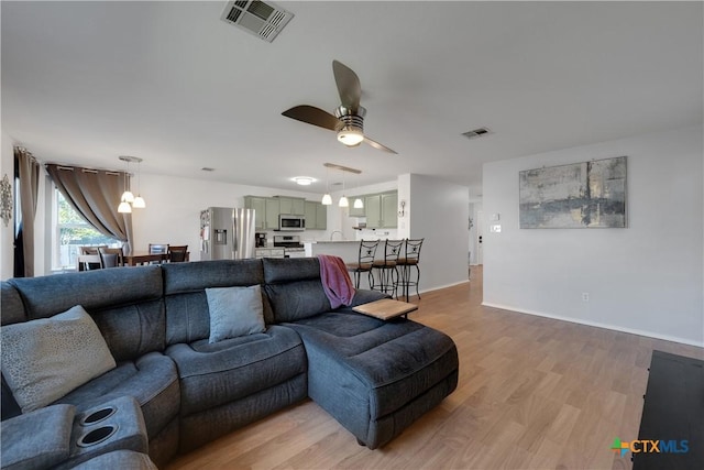 living area featuring visible vents, baseboards, light wood-type flooring, and ceiling fan with notable chandelier
