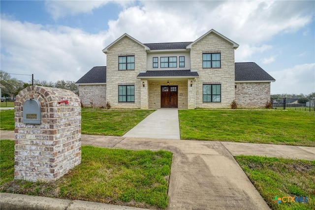 view of front facade with stone siding, a shingled roof, a front yard, and fence