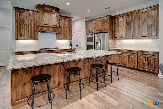 kitchen featuring custom range hood, light wood-type flooring, appliances with stainless steel finishes, and a sink