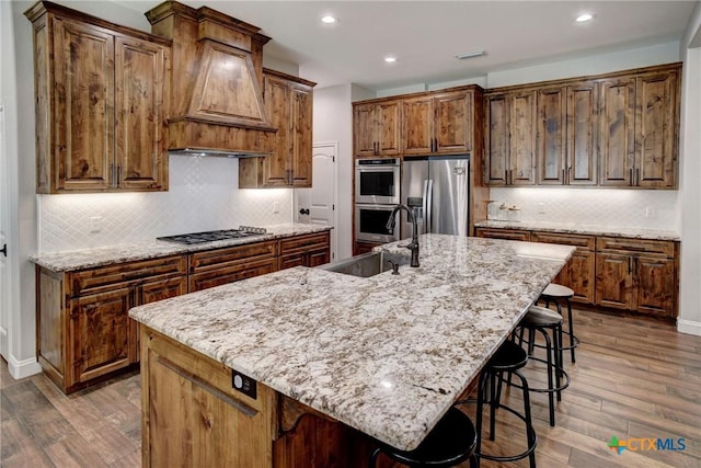 kitchen featuring wood finished floors, a breakfast bar, custom exhaust hood, a sink, and appliances with stainless steel finishes