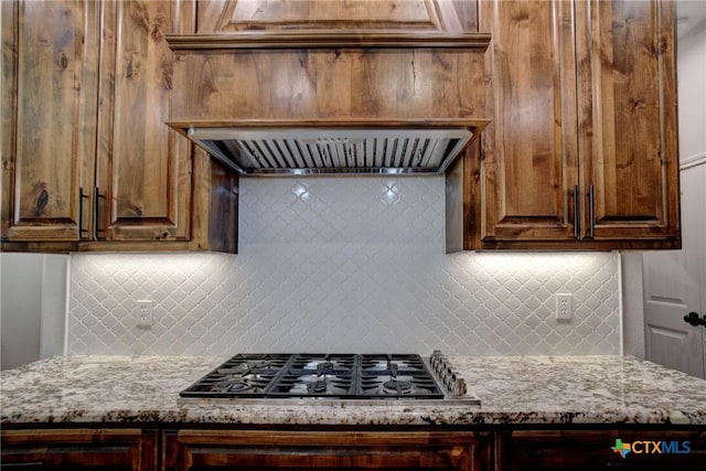 kitchen featuring light stone counters, backsplash, exhaust hood, and stainless steel gas cooktop