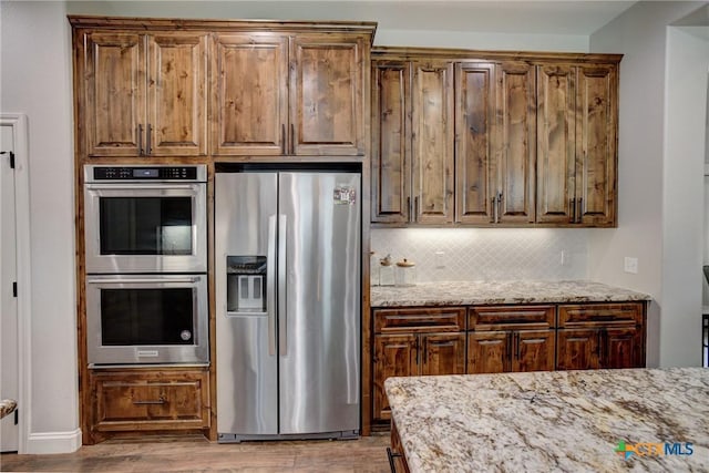 kitchen featuring light stone counters, stainless steel appliances, tasteful backsplash, and wood finished floors