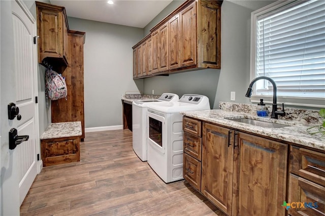 clothes washing area featuring baseboards, light wood-type flooring, cabinet space, independent washer and dryer, and a sink