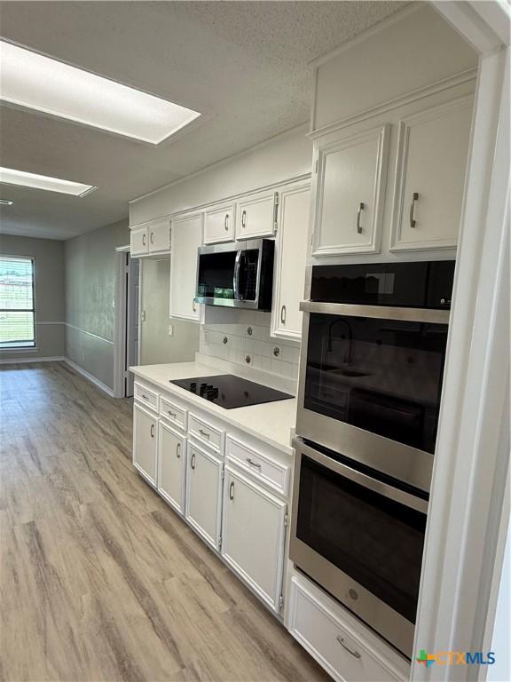 6601 Wells Fargo Rd, Killeen, TX 76542 - kitchen with stainless steel appliances, light wood-style flooring, light countertops, white cabinetry, and tasteful backsplash