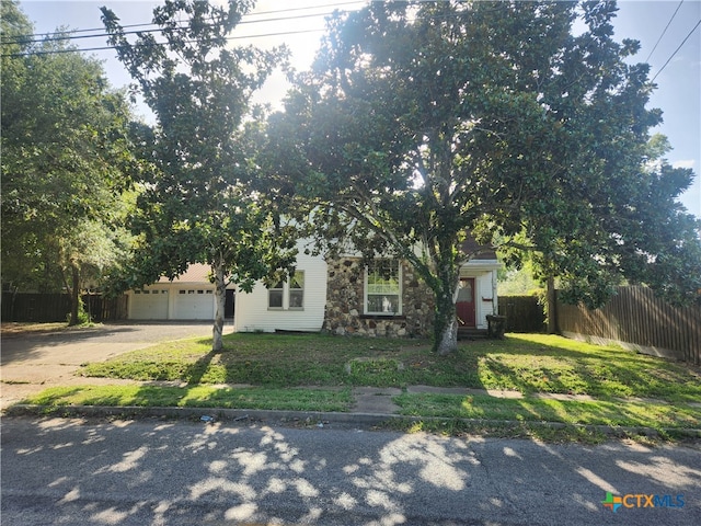 view of property hidden behind natural elements featuring a garage and a front yard