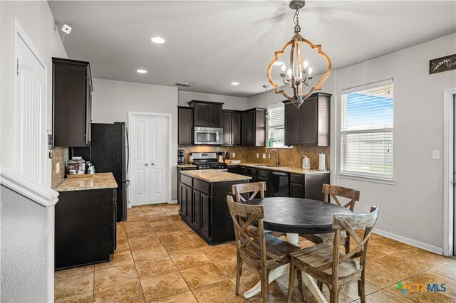 interior space with a center island, tasteful backsplash, a sink, appliances with stainless steel finishes, and a notable chandelier