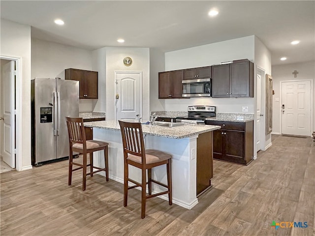 kitchen with sink, light hardwood / wood-style flooring, an island with sink, appliances with stainless steel finishes, and a kitchen bar