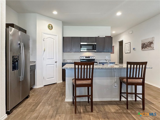 kitchen featuring light stone countertops, stainless steel appliances, light hardwood / wood-style flooring, a kitchen island with sink, and a breakfast bar