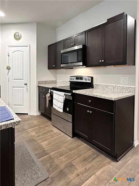 kitchen featuring dark brown cabinets, light stone counters, light wood-type flooring, and stainless steel appliances